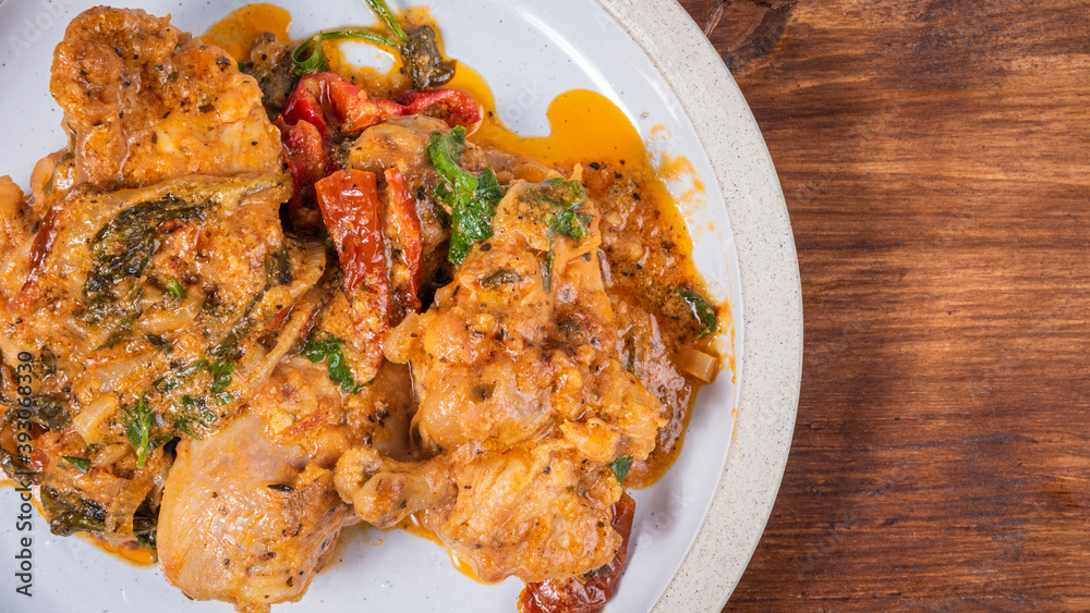 Ready Italian dish - Tuscan chicken with dried tomato and cream sauce with cheese and onions on a plate on a wooden table, top view, close-up, copy space Ready Italian dish - Tuscan chicken with dried tomato and cream sauce with cheese and onions on a plate on a wooden table, top view, close-up, copy space