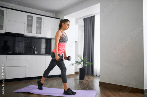 Fit young woman practicing lunges with weight at home.
