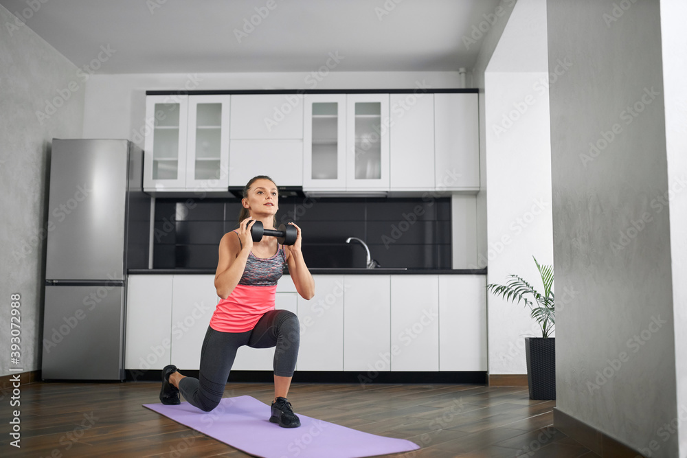 Fit young woman practicing lunges at home using dumbbell. Fit young woman practicing lunges at home using dumbbell.
