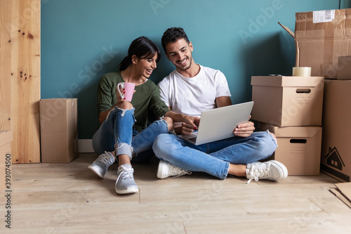 Beautiful young couple looking decoration ideas with laptop while drinking a cup of coffee sitting on the floor at home. photo