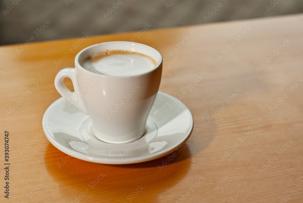 White coffee cup on a wooden board. Blurred bar interior on background. Free space near the coffee.