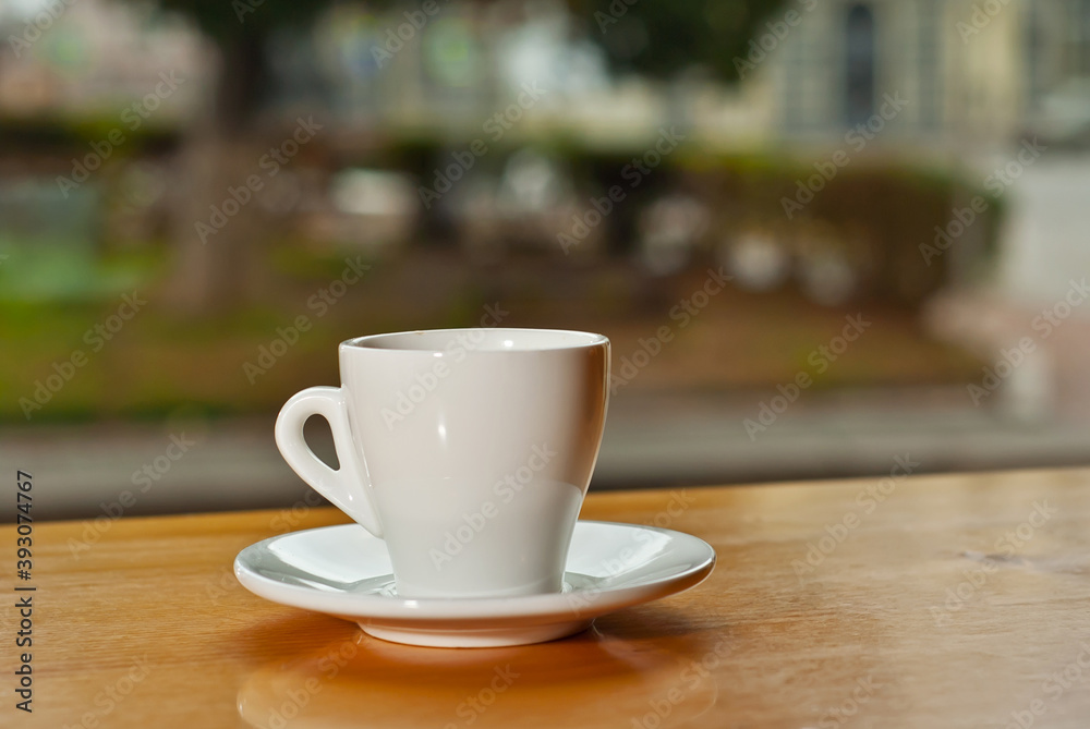 White coffee cup on a wooden board. Blurred bar interior on background. Free space near the coffee.