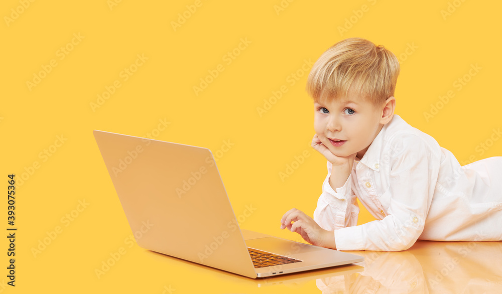Litttle child boy using laptop on yellow background. Education, online study, home studying, distance learning. Primary school student during quarantine Litttle child boy using laptop on yellow background. Education, online study, home studying, distance learning. Primary school student during quarantine