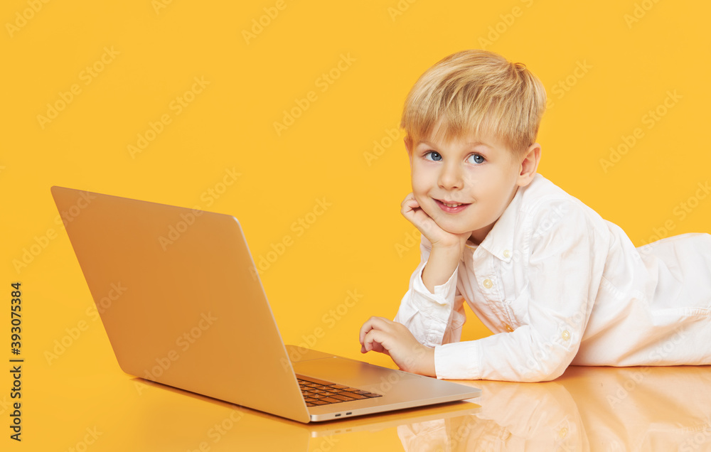Litttle child boy using laptop on yellow background. Education, online study, home studying, distance learning. Primary school student during quarantine Litttle child boy using laptop on yellow background. Education, online study, home studying, distance learning. Primary school student during quarantine