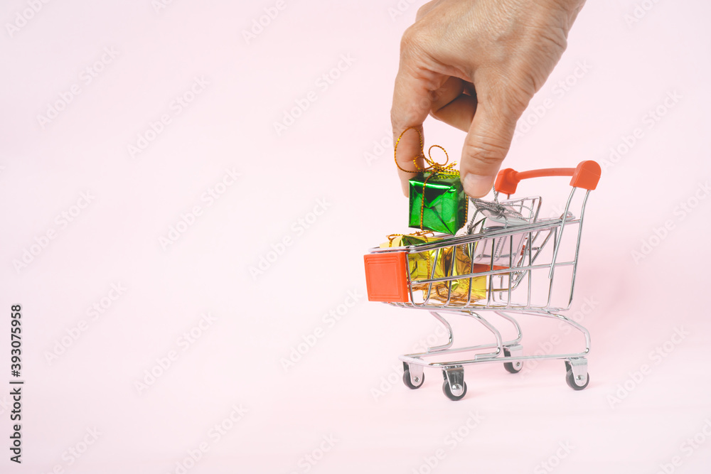 Fototapeta premium human's hand holding green small gift box in shopping cart on sweet pink background