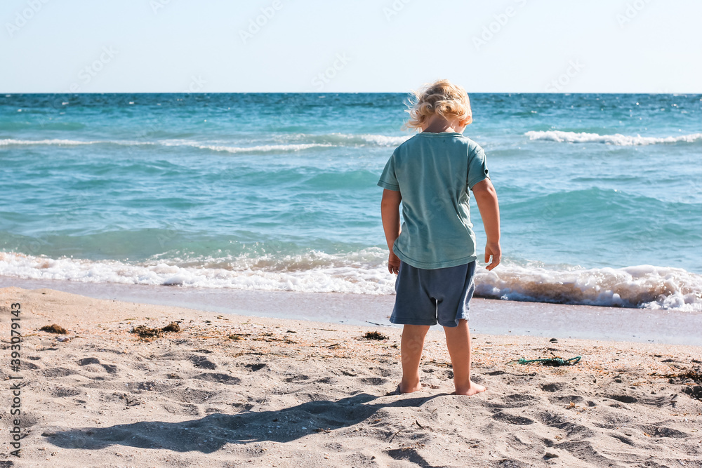 Little boy walking and playing alone on the beach. Summertime, vacation, travel, nature concept.