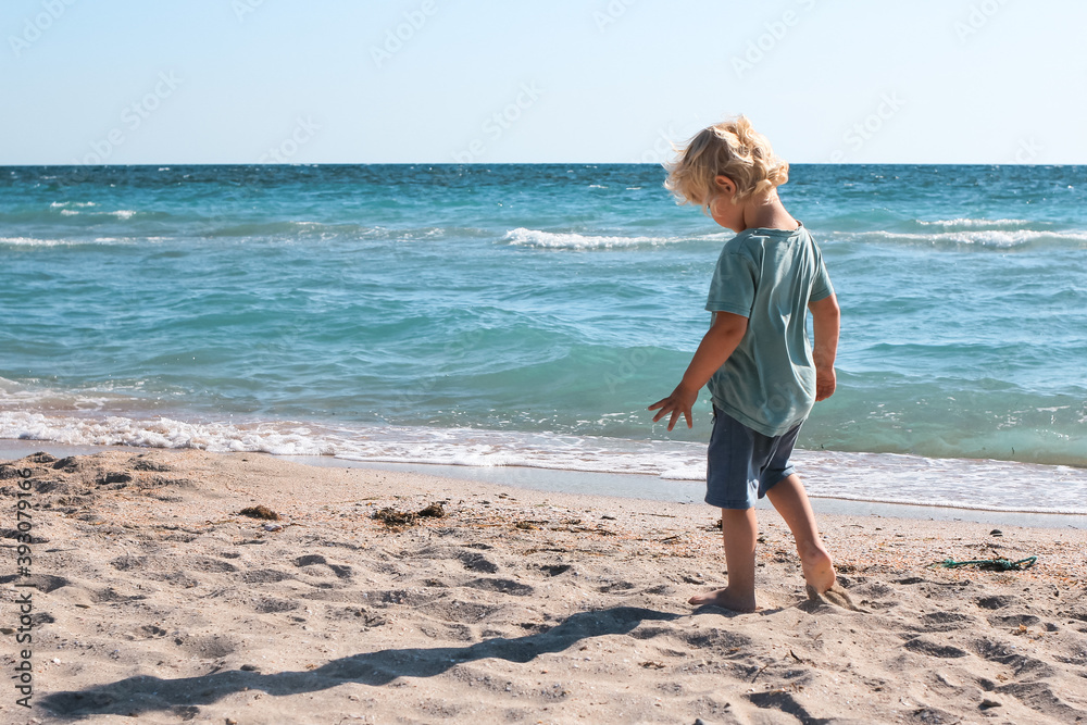 Little boy walking and playing alone on the beach. Summertime, vacation, travel, nature concept.