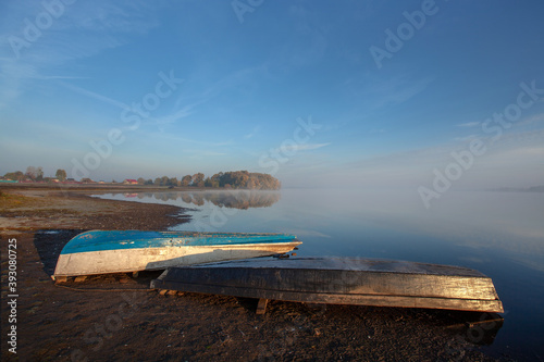 Fototapeta Naklejka Na Ścianę i Meble -  Foggy dawn over the lake. Overturned boats on the shore.