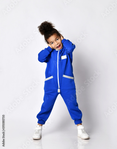 Happy screaming emotional dark-skinned kid girl in blue trendy jumpsuit performs hip-hop modern dance aerobics