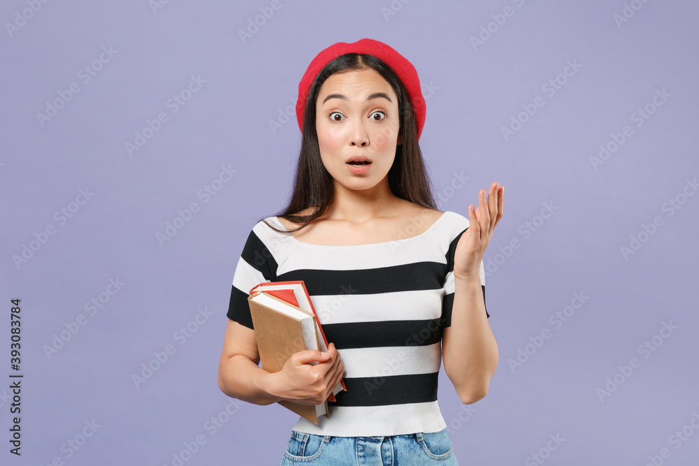 Shocked amazed young brunette asian student woman 20s wearing striped t-shirt red beret standing hold books spreading hands looking camera isolated on pastel violet colour background studio portrait. Shocked amazed young brunette asian student woman 20s wearing striped t-shirt red beret standing hold books spreading hands looking camera isolated on pastel violet colour background studio portrait.