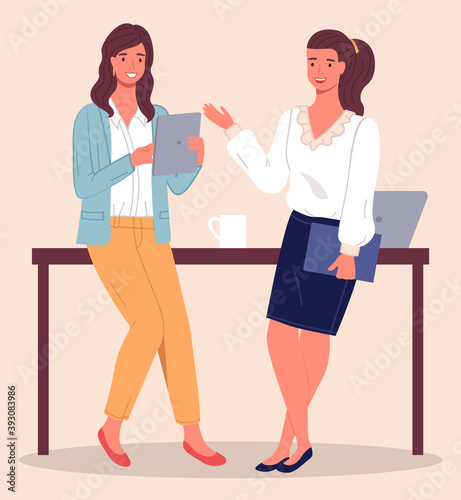 Two modern women, office workers, clerks or colleagues communicate, leaning on the table. Woman with tablet in her hand, girl with folder in her hand. Laptop and cup on the table. Coffee break
