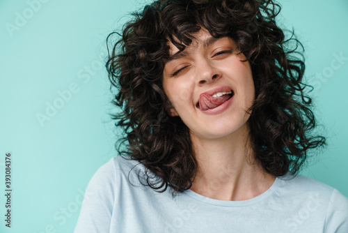 Joyful beautiful curly girl winking and showing her tongue