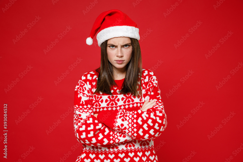 Dissatisfied young brunette Santa woman 20s in sweater, Christmas hat holding hands crossed isolated on bright red colour background, studio portrait. Happy New Year celebration merry holiday concept. Dissatisfied young brunette Santa woman 20s in sweater, Christmas hat holding hands crossed isolated on bright red colour background, studio portrait. Happy New Year celebration merry holiday concept.