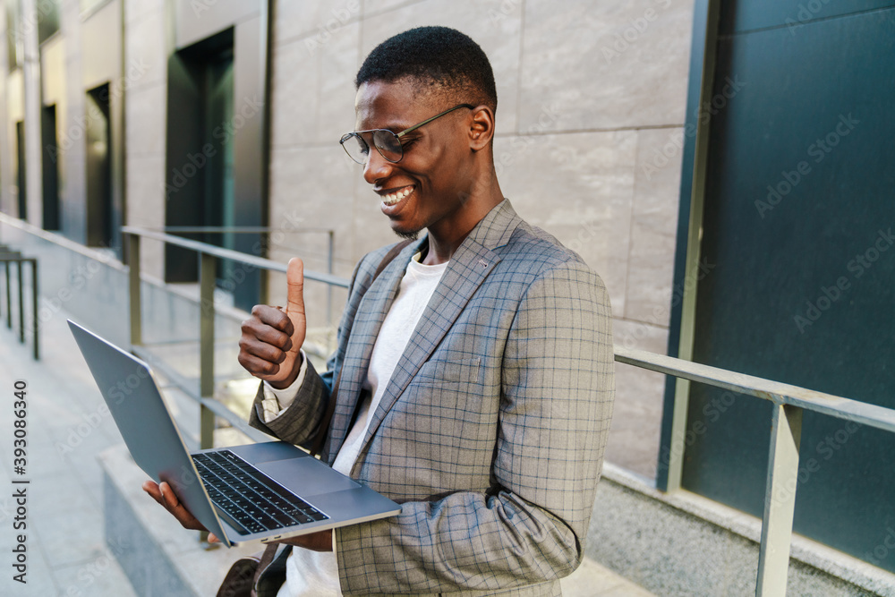 Joyful african american man showing thumb up and using laptop Joyful african american man showing thumb up and using laptop