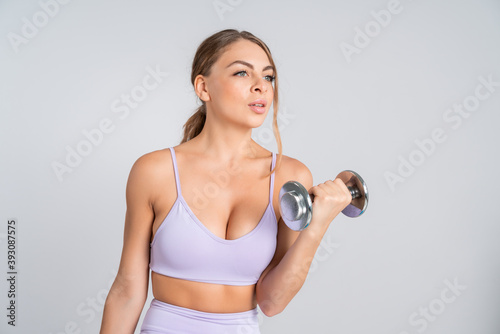 Portrait of attractive young fit woman in pink sport top and pants losing weight and doing exercises with heavy metal dumbbell.