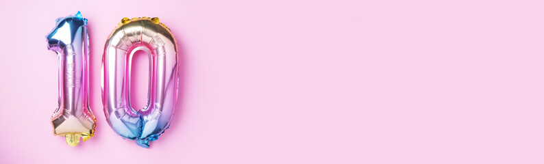 Rainbow foil balloon number, digit ten. Birthday greeting card with inscription 10. Anniversary concept. Top view. Colored numeral on pink background. Numerical digit, Celebration event, template