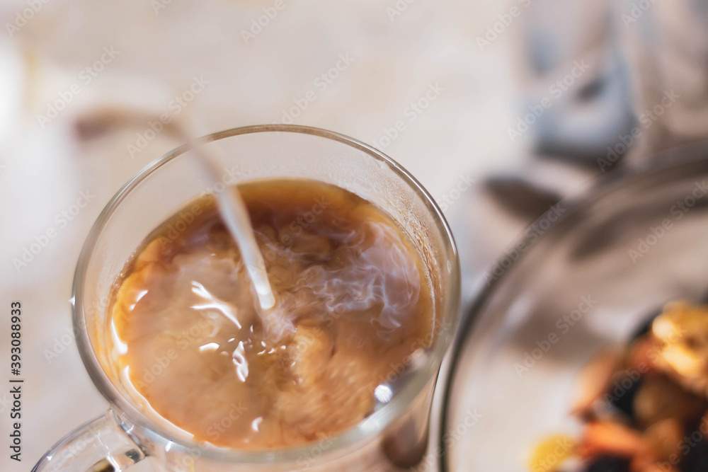 Pour the milk into a glass cup of coffee, macro photo of beautiful coffee divorces with milk. Pour the milk into a glass cup of coffee, macro photo of beautiful coffee divorces with milk.