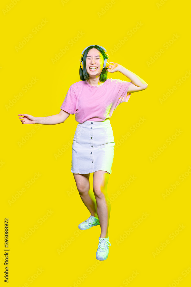Young asiatic woman having fun isolated on yellow background listening music Young asiatic woman having fun isolated on yellow background listening music
