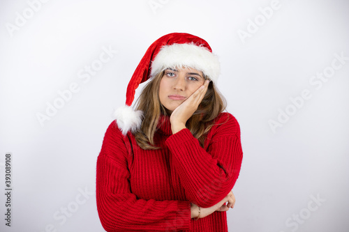 Young pretty blonde woman wearing a red casual sweater and a christmas hat over white background thinking looking tired and bored with crossed arms