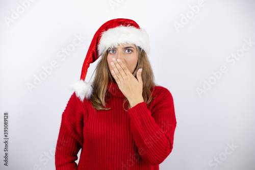 Young pretty blonde woman wearing a red casual sweater and a christmas hat over white background surprised covering the mouth