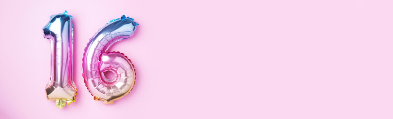 Creative layout. Rainbow foil balloon number, digit sixteen. Birthday greeting card with inscription 16. Anniversary concept. Top view. Stylish colored numeral on pink background. Numerical digit