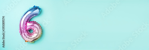 Creative layout. Rainbow foil balloon number and digit six 6. Birthday greeting card. Anniversary concept. Top view. Copy space. Stylish colored numeral over blue background. Numerical digit.