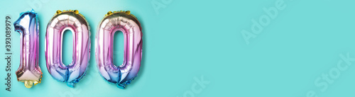 Rainbow foil balloon number, digit one hundred. Birthday greeting card with inscription 100. Anniversary concept. Top view. Colored numeral on blue background. Numerical digit, Celebration event