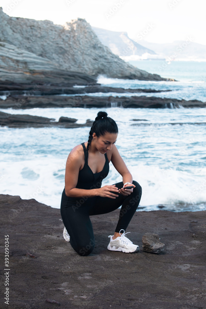 young woman looking at cell phone while practicing squat exercise outdoors