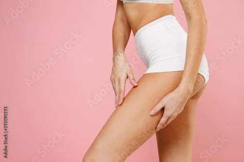 Cropped image side view of beautiful young woman 20s wearing white brassiere underwear with strong sports body standing posing hold hands on legs isolated on pastel pink background, studio portrait.