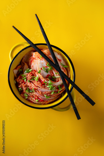Kimchi cabbage in a bowl with chopsticks on a colored background, top view, Korean cuisine. Trend food photography