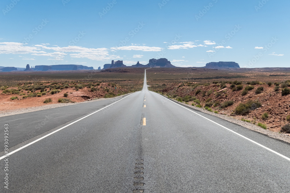 Route with a straight view to the most iconic view of Monument Valley National Park with a cloudless sky at Utah, United States. Some clouds can be seen on the horizon
