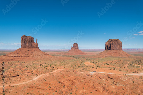 Dirty road passes by the most iconic view of Monument Valley National Park with a cloudless sky at Utah, United States.