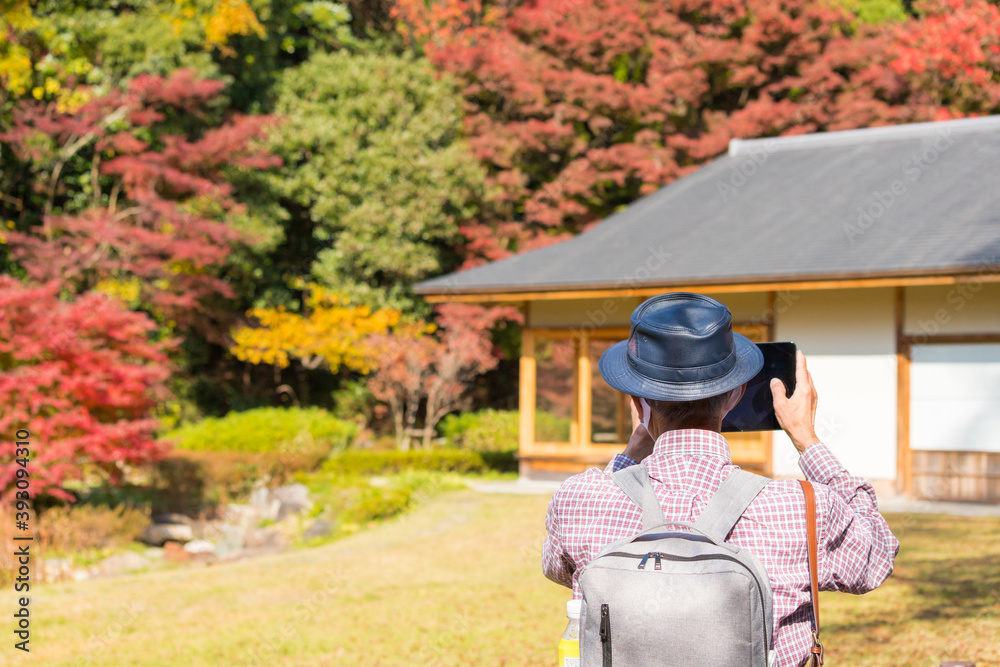 秋の公園でマスクを付けて日本庭園の風景を撮影している男性の姿