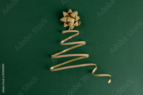 Christmas tree made from gold ribbon on a bright green backdrop. Merry Christmas and Happy New Year festive background with empty space for text.