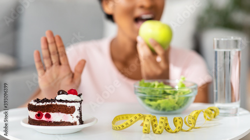 Unrecognizable black woman eating fresh apple and refusing unhealthy cake  blank space