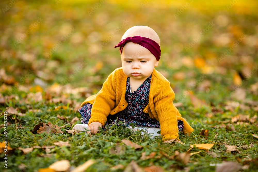 A little girl 1 year old dressed in a yellow shirt and a white hat sits in a grey stroller in the park. A little girl 1 year old dressed in a yellow shirt and a white hat sits in a grey stroller in the park.