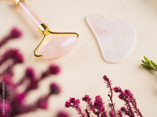 Fototapeta Naklejka Na Ścianę i Meble -  Pink quartz guasha face roller on floral background. Chinese beauty massage tool.