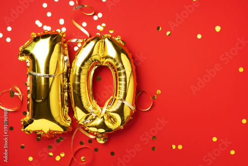 Gold foil balloon number, digit ten. Birthday greeting card with inscription 10. Anniversary celebration event. Banner. Golden numeral, red background. Numerical digit, bright shiny glitter photo