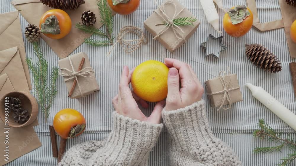 A girl in a knitted sweater holds a tangerine in her hands, surrounded by Christmas gifts. Christmas concept, new year's holiday atmosphere. Craft paper gift wrapping handmade. A girl in a knitted sweater holds a tangerine in her hands, surrounded by Christmas gifts. Christmas concept, new year's holiday atmosphere. Craft paper gift wrapping handmade.