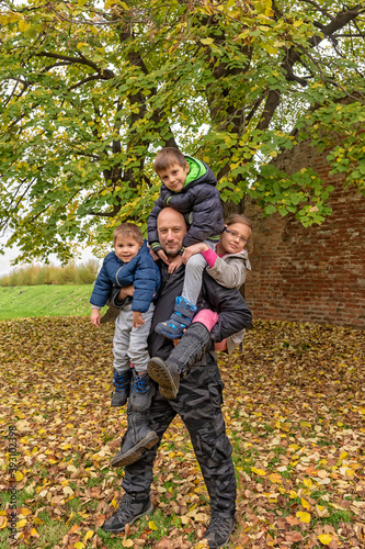 The father is carrying three children. Father carrying childs piggyback. The father plays with the childrens on an autumn day