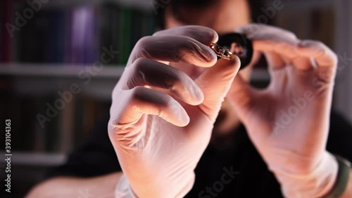 Professional jewelry appraiser is holding gold ring and examining it through magnifier glass. Young caucasian man is evaluating bijou with the help of loupe sitting in pawnshop. Precious metals theme.