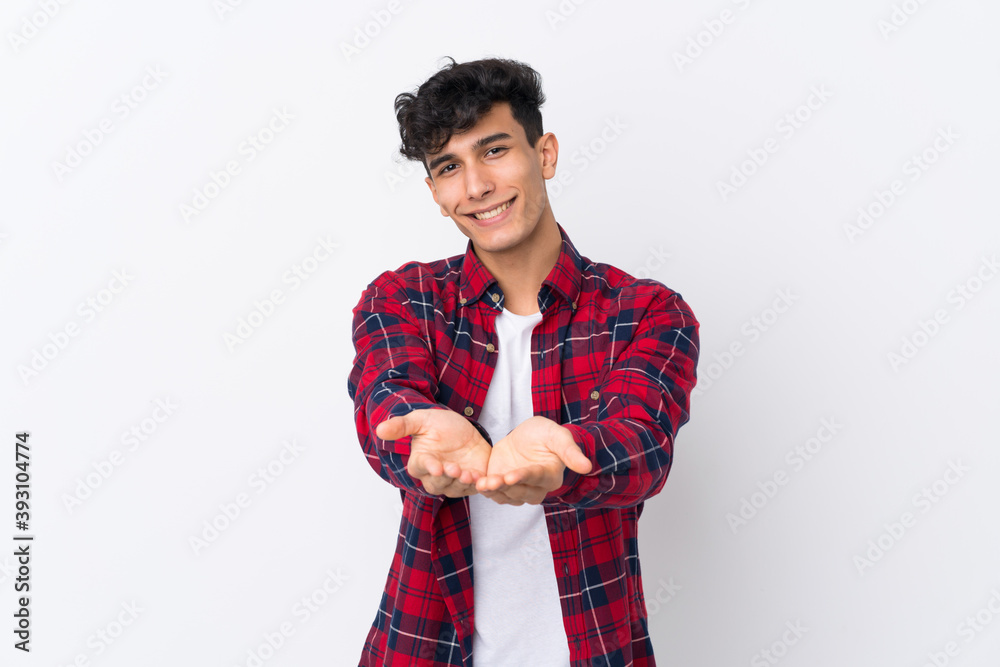 Young Argentinian man over isolated white background holding copyspace imaginary on the palm to insert an ad Young Argentinian man over isolated white background holding copyspace imaginary on the palm to insert an ad