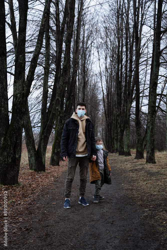 dad and son stand in the middle of the park, looking to the side, medical masks on their faces as a precaution, viral epidemic, single father, father hugs son