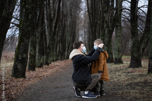 one parent puts on a medical mask on a young son, a young dad walks with his son in the park, winter park, autumn truancy, unconventional family © Maxim