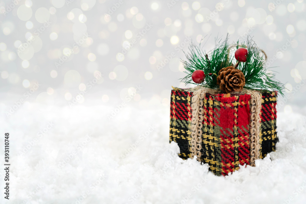 Winter Christmas composition on a white background. A red gift decorated with a spruce branch, a pine cone and red berries stands on white snow. Bokeh in the background. Close-up Winter Christmas composition on a white background. A red gift decorated with a spruce branch, a pine cone and red berries stands on white snow. Bokeh in the background. Close-up