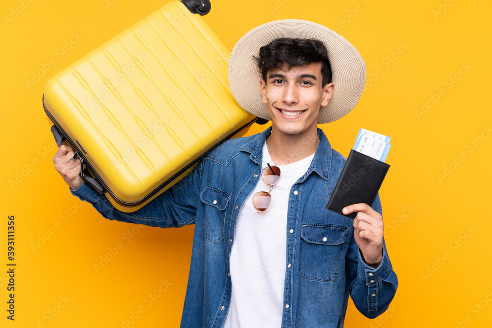 Young Argentinian man over isolated yellow background in vacation with suitcase and passport Young Argentinian man over isolated yellow background in vacation with suitcase and passport