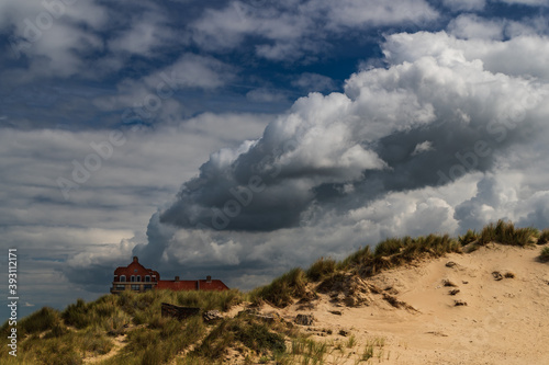 From the ruined dunes, you can see a large building with a red roof and clouds that seem to come out of the building like sails on a boat.