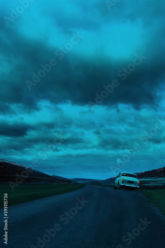 Vintage car parked along country road under dark cloudy sky.
