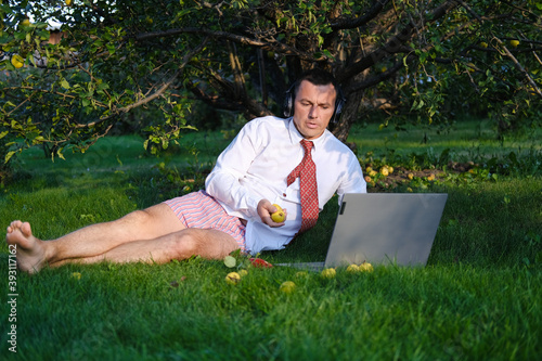 фотографія Male manager working in the garden, lying on the lawn, holding an online meeting