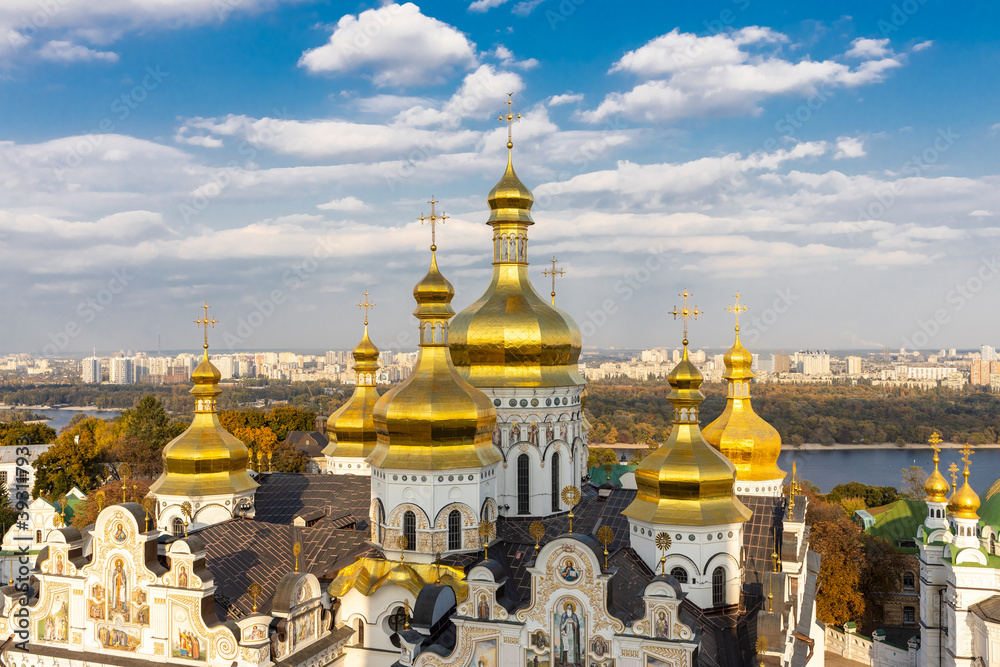 Beautiful yellow and gold domes of the Orthodox Church against the background of the blue sky and the city. Domes of the Assumption Cathedral of the Kiev-Pechersk Lavra.